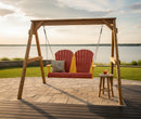 The Kanyon Living Poly Lumber 4′ Adirondack Swing in red and yellow by Kanyon Living seats two and hangs from a wooden frame on a stone patio overlooking a lake—perfect outdoor furniture for relaxing with scenic views.