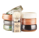 DDR BBQ Supply Immaculate Beard shave brush in clear packaging surrounded by a stack of rustic ceramic shaving bowls.