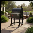 The Smokin Brothers "24" Premier Plus Pellet Grill by Smokin Brothers, a black insulated pellet smoker with wheels, sits on a patio amid green bushes and outdoor furniture on a sunny day.