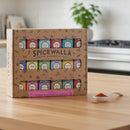 The Spicewalla Kitchen Essentials 18-Pack Collection sits on the counter, showcasing its colorful spice tins. Two white ceramic spoons hold vibrant ground spices, while a stove in the background highlights these essentials from Spicewalla.