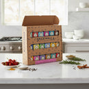 A Spicewalla Kitchen Essentials 18-Pack Collection rests on a white kitchen counter with fresh herbs and spices nearby, while a modern stove and bowls by Spicewalla complete the stylish cooking space.