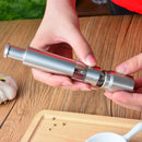 A person uses DDR BBQ Supply Thumb Grinders by DDR BBQ Supply over a wooden table with garlic and a cutting board nearby—an essential BBQ accessory for easy, one-handed seasoning.