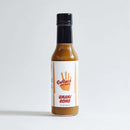 A bottle of Culture Hot Sauce Umami Bomb from Culture Hot Sauce stands upright against a plain white background. The label showcases an orange handprint and bold, straightforward text, emphasizing this uniquely savory hot sauce crafted with natural umami ingredients.