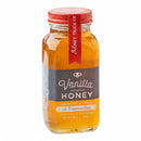 A glass jar of Honey Truck Co Raw Florida Vanilla Infused Honey, topped with a red-sealed lid, features vibrant black and yellow label accents highlighting its Florida origin and infusion with Madagascar vanilla beans. The golden raw honey glows inside the jar, offering a striking presentation from Honey Truck Co.