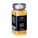 A glass jar of The Spice Lab Scotch Bonnet Sea Salt, featuring a silver lid and black label, holds a vibrant orange and red seasoning blend that offers bold Caribbean-inspired heat as a spicy finishing salt.