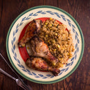 A plate with three roasted chicken drumsticks, seasoned with The Spice Lab Organic Whole Thyme, and a serving of rice mixed with corn and peas, placed on a wooden table with a fork and knife beside the plate.