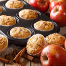 Freshly baked apple muffins in a muffin tin and on a wooden table, surrounded by red apples and cinnamon sticks, fill the air with the warm aroma of The Spice Lab Apple Pie Spice Blend, making them the perfect seasonal spice treat for any baking enthusiast.