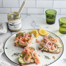 Open-faced sandwiches with smoked salmon, shrimp, cucumber, red onion, and dill on a white plate. Nearby are lemon wedges, green glasses, a striped napkin, and a jar of Terrapin Ridge Farms Dill Pickle Mustard.