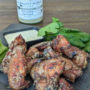 Grilled chicken wings with a small cup of dipping sauce and fresh herbs, served on a dark plate atop a wooden table. In the background is a bottle of Terrapin Ridge Farms Dill Pickle Mustard.