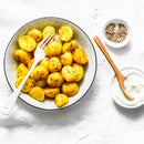 A bowl of seasoned roasted potatoes, brightened with The Spice Lab Organic Ground Turmeric for a golden color inspired by Indian cuisine, is served alongside a white fork, a dish of mixed pepper, and a bowl of sour cream with a wooden spoon—all set on a white tablecloth.