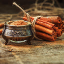 A bundle of cinnamon sticks tied with twine sits next to a small ornate bowl filled with aromatic The Spice Lab Organic Ground Vietnamese Saigon Cinnamon, displayed on a rustic wooden surface.