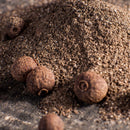 The Spice Lab Organic Ground Allspice by The Spice Lab is pictured as a small mound beside whole allspice berries on a rustic dark surface—ideal for adding rich, aromatic flavor to your Jamaican jerk seasoning or homemade BBQ sauce.