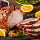 Sliced glazed ham garnished with pineapple rings and orange slices on a dark serving platter, delicately infused with baking spice and The Spice Lab Organic Ground Ginger, with green beans and cranberry sauce visible in the background.
