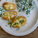 Baked potatoes with melted cheese and The Spice Lab Organic Whole Dill Weed, served alongside a cucumber salad seasoned with The Spice Lab Organic Whole Dill Weed and creamy tzatziki dressing, presented on a white plate.