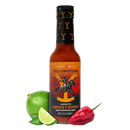A bottle of Elijah's Xtreme Ranchers Revenge (Ghost Pepper) hot sauce from Elijah's Xtreme stands between a whole lime, lime wedges, and a red chili pepper on a white background.