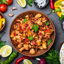 A bowl of chili with beans, chicken, and vegetables is surrounded by fresh ingredients like tomatoes, peppers, onions, lime wedges, parsley, and tortillas on a gray surface. A sprinkle of The Spice Lab Chile de Arbol Powder from The Spice Lab adds a zesty kick to this vibrant dish—perfect for bulk foodservice or any hearty gathering.