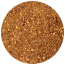A close-up view of a circular pile of mixed spices, including coarse salt, pepper, red chili flakes, and other seasonings, enhanced with The Spice Lab Scotch Bonnet Sea Salt by The Spice Lab for a vibrant Caribbean-inspired flavor, set against a white background.
