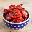 A blue and white patterned bowl filled with dried tomato slices, sprinkled with The Spice Lab Organic Oregano Leaf, sits on a wooden surface—bringing a hint of Italian cooking tradition to your kitchen.