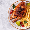 Grilled chicken with crispy fries, garnished with lime wedges and parsley, finished with a sprinkle of The Spice Lab Birdseye Chili Pepper Powder and accompanied by red chili peppers on a round plate, viewed from above.