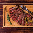 Sliced medium-rare steak garnished with coarse salt, The Spice Lab Organic Granulated Onion, and fresh herbs, served on a wooden board with a fork and knife.