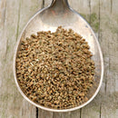A metal spoon filled with brown, oval-shaped The Spice Lab Whole Celery Seeds rests on a weathered wooden surface.