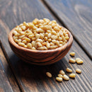 A wooden bowl filled with The Spice Lab Organic Pine Nuts sits on a rustic wooden surface, with a few pine nuts scattered beside the bowl—perfect as a salad topping or versatile baking ingredient from The Spice Lab.