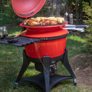 A red kamado grill with its lid open cooks corn and chicken, while utensils, a mason jar, and seasonings sit nearby. Perfect for backyard grilling using the Flame Boss 400 WiFi Kamado Smoker Controller Kit by Flame Boss for precision control.