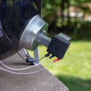 A close-up of the Flame Boss 400 WiFi Universal Smoker Controller Kit by Flame Boss, with its fan and probes attached to a round charcoal grill outdoors, wires connected to temperature probes, and a grassy yard in the background.