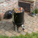 The Flame Boss 400 WiFi Universal Smoker Controller Kit by Flame Boss is installed on a black barrel smoker grilling vegetables, muffins, and a roast on a stone patio near two potted plants and a brick wall; the grill lid rests nearby.