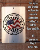 Metal sign with 'Made in the USA' and American flag design on a wooden background.