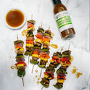 Five vegetable skewers with peppers, red onion, mushrooms, and squash are arranged on a white surface beside a bowl of sauce and a quart bottle of Terrapin Ridge Farms Ginger, Miso & Honey Dressing.