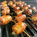 Bacon-wrapped jalapeño poppers cooking over an open flame, glazed with Brushfire Farms Brushfire Glaze for a sweet heat finish, secured with toothpicks for a spicy Margarita-inspired, crispy bite.
