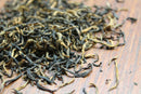Loose leaf World Spice Golden Monkey black tea from World Spice, featuring golden tips scattered on a wooden surface, showcases twisted and wiry dried tea leaves from Fujian Province. This strong-bodied tea exemplifies remarkable craftsmanship in every leaf.
