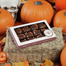 A Millican Pecan Dark Chocolate Caramillicans Gift Box—featuring gourmet chocolate caramel pecan candy by Millican Pecan—rests on a hay bale, surrounded by pumpkins, a white skull decoration, and autumn leaves to create a festive fall atmosphere.