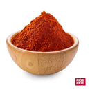 A wooden bowl brimming with vibrant red Rico Rico Guajillo Chile Powder Shaker, celebrated for its mild heat and signature chili flavor, sits against a white background. The bold RICO RICO logo appears in the bottom right corner, emphasizing its roots in authentic Mexican cuisine.