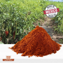 A pile of reddish-brown Rico Rico Guajillo Chile Powder Shaker sits on a white surface, with chili plants in the background and a "Made in Mexico" label in the top right corner, highlighting its authentic Mexican origin. Brought to you by Rico Rico, this vibrant spice is perfect for those who enjoy mild heat chili, adding depth and rich flavor to your favorite dishes.
