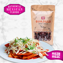 A plate of chilaquiles garnished with cheese and cilantro is placed beside a bag from the Rico Rico Dried Mexican Chiles 3-Pack – Ancho, Guajillo & Arbol Peppers. The vibrant pink labels display "Authentic Mexican Flavor" and "Rico Rico!" against a marble background.