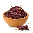 A wooden bowl filled with Rico Rico Guajillo Dried Chiles – Authentic Medium Heat Mexican Peppers, with two additional dried chilies from Rico Rico placed beside the bowl on a white background.