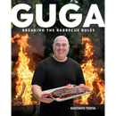 A smiling man in a black shirt holds a tray of grilled meat, standing in front of two flaming grills. Large text reads "Guga: Breaking the Barbecue Rules - Hardcover" by Books by splitShops at the bottom, inspired by Gustavo Tosta’s popular Guga Foods channel and creative barbecue recipes.