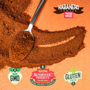 A spoon filled with Rico Rico Habanero Chile Powder Shaker is spilled on an orange surface, featuring non-GMO, 100% authentic product, and gluten-free labels at the bottom. “Rico Rico Habanero Chile Powder!” appears at the top right—perfect for adding bold hot spice to your favorite dishes.