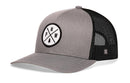 The Haka Hat PNW Trucker Hat features a gray-black design, mesh back panels, and a front patch with crossed lines, the letters PNW, and a pine tree. This snapback blends classic style with Pacific Northwest vibes.