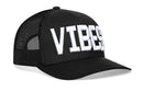 The Haka Hat VIBES Trucker Hat is a black snapback with white "VIBES" embroidery on the front and a comfort-fit sweatband for all-day wear.
