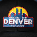 A close-up of the Haka Hat Denver Mile High City Trucker Hat | Black Cityscape Snapback by Haka Hat, featuring a colorful 3D embroidered patch with "Mile High City Denver Colorado," a city skyline, mountains, and a yellow sun.
