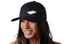 A woman with long brown hair smiles while wearing the Haka Hat Cornhole Board Trucker Hat | Black Bags Snapback by Haka Hat, which features an embroidered cornhole board graphic. The background is plain white.