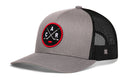 The Haka Hat Carolina Hockey Trucker Hat | Black CAR X Snapback by Haka Hat features a gray front panel and brim, black mesh back, and a red and black circular patch with crossed hockey sticks and the letters C A R. This signature 5.0 trucker is the perfect North Carolina hat for hockey fans.