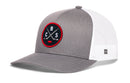 The Haka Hat Columbus Hockey Trucker Hat | CBS X Snapback features a gray and white trucker design with a mesh back and an eye-catching round black patch embroidered on the front, displaying crossed baseball bats, the letters B and C, and a striking red border. A small woven tag decorates the cap’s side—making it the perfect standout hat for Columbus hockey fans.
