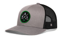 The Haka Hat Dallas Hockey Trucker Hat | DAL X Snapback by Haka Hat features a gray and black trucker design with a circular green and black DAL X embroidered patch on the front, showcasing two crossed hockey sticks along with the letters D, A, and L. This snapback includes a mesh back and an adjustable closure for a comfortable fit.