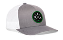 Check out the Haka Hat Dallas Hockey Trucker Hat | DAL X Snapback: a gray and white mesh-back trucker hat by Haka Hat, featuring a circular green and black embroidered DAL X patch with crossed hockey sticks and the letters D, A, and L on the front.