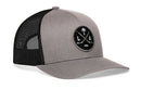 Haka Hat Los Angeles Hockey Trucker Hat with a gray front, black mesh back, and a circular LA X patch featuring crossed hockey sticks, a palm tree, and a hockey puck.