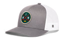 Introducing the Haka Hat Minnesota Hockey Trucker Hat | MIN X Snapback by Haka Hat—a gray and white mesh baseball cap featuring a green circular patch on the front with two crossed hockey sticks, a puck, and the letters M and N. This stylish Minnesota hockey trucker hat also includes a small stitched logo tag on the side panel.